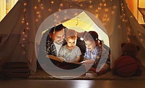 Happy family father and children reading a book in tent at hom
