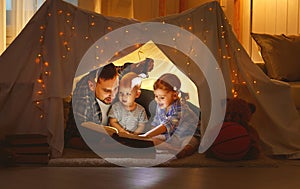 Happy family father and children reading a book in tent at hom