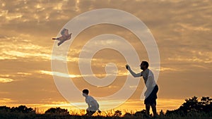 Happy family father and children running in the meadow with a kite in summer at sunset