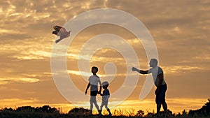 Happy family father and children running in the meadow with a kite in summer at sunset