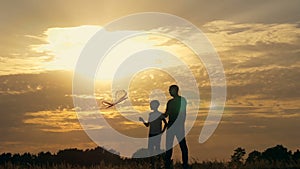 Happy family father and children running in the meadow with a kite in summer at sunset