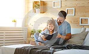 Happy family father and daughter reading book in bed