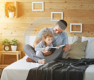 Happy family father and daughter reading book in bed