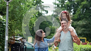 A happy family. Father keeps his daughter on his shoulders. He tilts the girl to mom and they laugh happily. hair