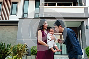 happy family, father kissing newborn baby while mother holding her standing in front of their house