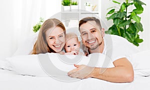 Happy family of father, mother and baby playing in bed