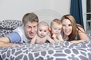 Happy family of father, mother and baby playing in bed