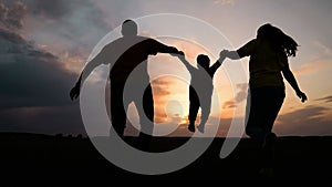 happy family. father mother and baby run play at sunset silhouette holding hands and throw up. happy family in kid dream