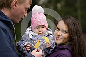 Happy family: Father, Mother and child - in autumn park: dad, mammy baby posing outdoor, girl holding in the hands of