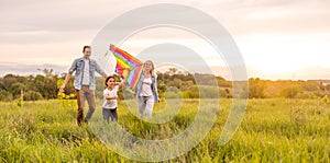 Happy family father, mother and child daughter launch a kite on nature at sunset