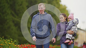 Happy family: Father, Mother and child - little girl in autumn park: walks in the alley with flowers