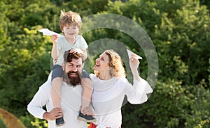 Happy family - father mother and child on meadow with a toy paper airplane in the summer on the nature background. Dad