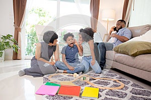 Happy family father and mother and children doing activity playing toy railway with fun in the living room.