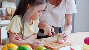 Happy family with father, mother and daughter in kitchen while mother chop apple fruit together at home.