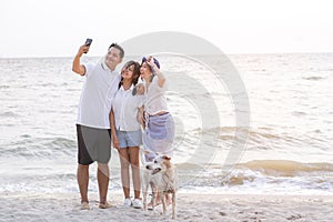 Happy Family with father mother and daughter selfie and looking smartphone and having fun on a tropical beach with dog. Family