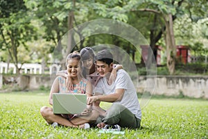 Happy family father, mother and daughter sitting on the grass and playing laptop