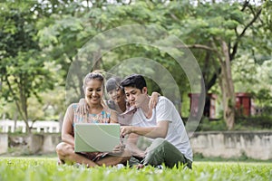 Happy family father, mother and daughter sitting on the grass and playing laptop