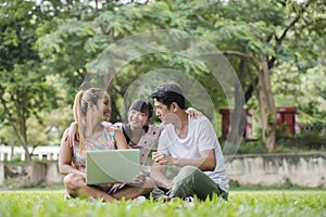 Happy family father, mother and daughter sitting on the grass and playing laptop