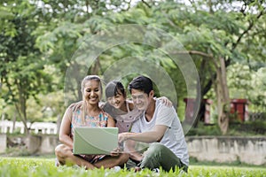 Happy family father, mother and daughter sitting on the grass and playing laptop