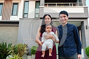 happy family, father and mother holding newborn baby standing in front of their house