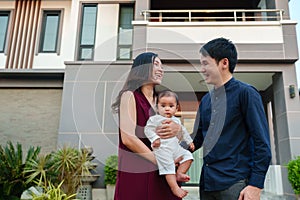 happy family, father and mother holding newborn baby standing in front of their house
