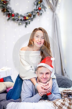 Happy family, father and mother in the morning in bedroom decorated for Christmas. Father in Santa`s hat laying on the bed and