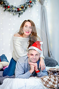 Happy family, father and mother in the morning in bedroom decorated for Christmas. Father in Santa`s hat laying on the bed and