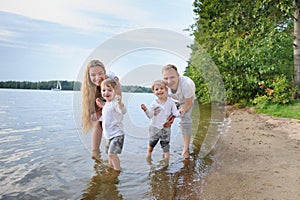 Happy family - father, mother, two sons on the beach with their feet in the water at sunset