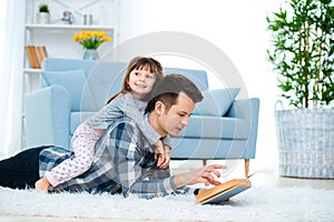 Happy family and father`s day concept. Dad with daughter spending time togetherness at home. Cute little girl on dad`s back lyin