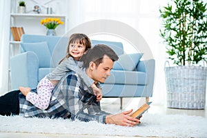 Happy family and father`s day concept. Dad with daughter spending time togetherness at home. Cute little girl on dad`s back lyin