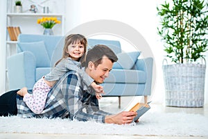 Happy family and father`s day concept. Dad with daughter spending time togetherness at home. Cute little girl on dad`s back lyin