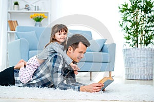 Happy family and father`s day concept. Dad with daughter spending time togetherness at home. Cute little girl on dad`s back lyin