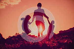 Happy family - father with son and daughter jumping from joy in sunset nature