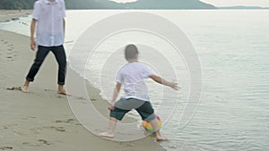 Happy family with father and son doing activity playing football on the beach for leisure