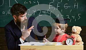 Happy family. Father and son doing homework together. Teacher in formal wear and pupil in mortarboard in classroom