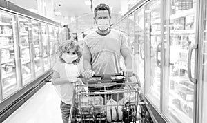 happy family of father and son in protection mask with shopping cart buying food, consumerism