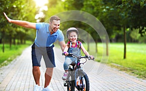 Happy family father teaches child daughter to ride a bike in the Park