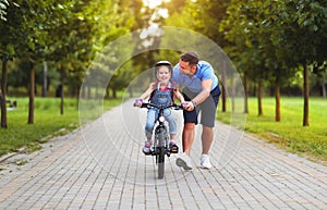 Happy family father teaches child daughter to ride a bike in the Park