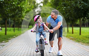 Happy family father teaches child daughter to ride a bike in the Park