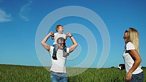 Happy family in the field on a Sunny day in the Park having fun and spending time together. The son sits on his father`s