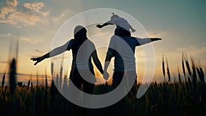 A happy family in a field on a walk enjoys the sunset. The child is sitting on the shoulders of a caring father. Mom and