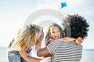 Happy family flying with kite and having fun on the beach - Multi ethnic couple playing with cheerful daughter on summer vacation