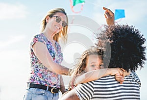 Happy family flying with kite and having fun on the beach - Multi ethnic couple playing with cheerful daughter on weekend vacation