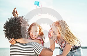 Happy family flying with kite and having fun on the beach - Multi ethnic couple playing with cheerful daughter on weekend vacation