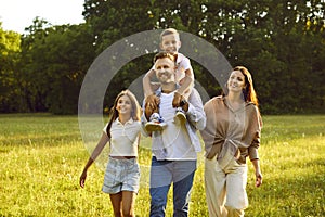 Happy family of four with kids walking in summer park enjoying beautiful nature.