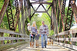 Happy Family of Four People Walking Dog Outside on Bridge photo