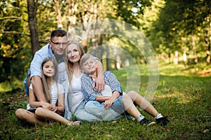 Happy family of four sitting on a grass in summer park outdoors and smiling