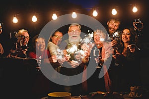 Happy family and friends celebrating with sparkler fireworks at home dinner - Different age of people having fun together in patio