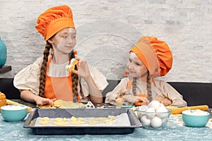 Happy family. Funny girls kids in orange chef uniform are preparing the dough, bake cookies in the kitchen. Sisters children enjoy