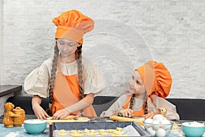 Happy family. Funny girls kids in orange chef uniform are preparing the dough, bake cookies in the kitchen. Sisters children enjoy